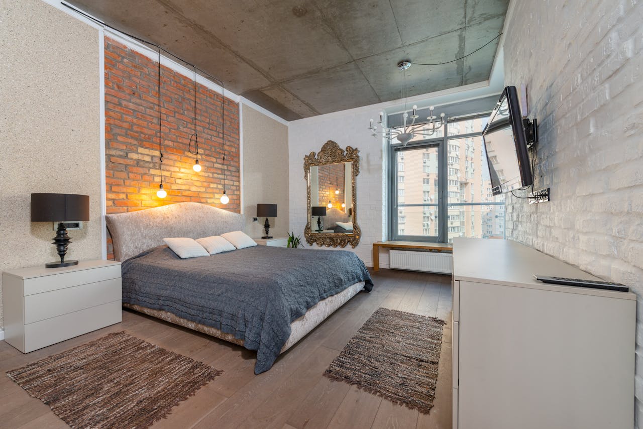 services-01 Spacious industrial-style bedroom with brick wall, cozy bed, and modern decor.